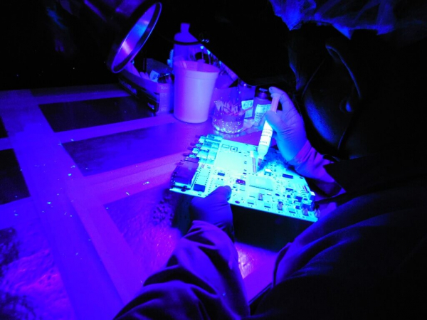 person in protective gear touches up the coating on a circuit board